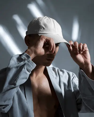 Artistic Cap Mockup With Male Model Adjusting Brim Under Dramatic Shadow Play