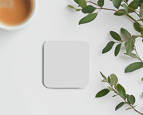 square-coaster-with-cup-amid-green-leaves-on-white-background