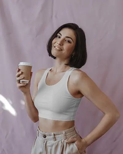 Indoor Crop Top Mockup Smiling Female Model In White Tank Holding Coffee Cup Against Light Purple Backdrop Casual Vibe