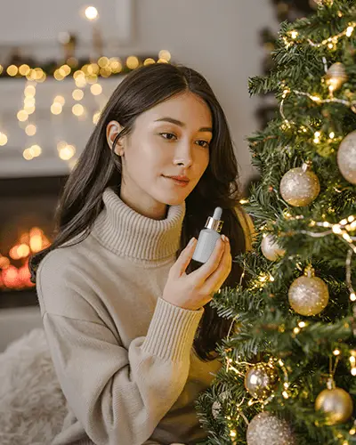 Holiday Dropper Bottle Mockup Female Model By Christmas Tree With Golden Lights