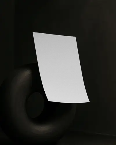 Curved Flyer Mockup Hovering Over Matte Black Sculpture Ring On Dark Backdrop With Soft Shadow Lighting