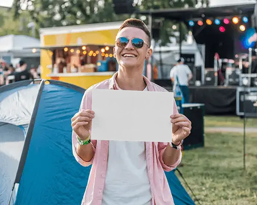 Music Festival Flyer Mockup Smiling Young Man In Sunglasses Holding Paper In Open Air Event Setting With Tent And Stage Background 098
