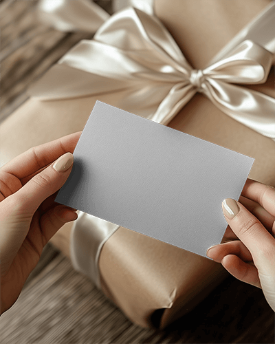 festive-greeting-card-mockup-hands-presenting-card-above-chic-gift-box-tied-with-silk-bow