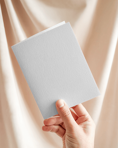 Hand Holding Greeting Card Mockup Against Beige Fabric Backdrop Textured Paper Soft Natural Light Warm Minimalist Scene