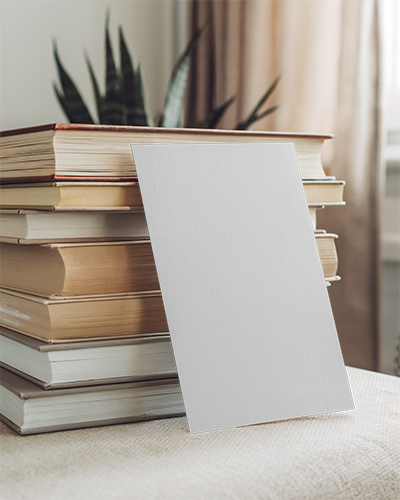 Cozy Bookstack Greeting Card Mockup Leaning Against Books In Soft Lit Room Warm Academic Vibe Homey Decor Setting