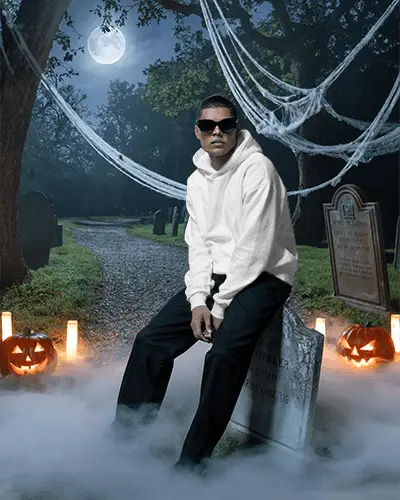 Eerie Halloween Mockup With Man In Hoodie Glasses Sitting On Gravestone Surrounded By Fog