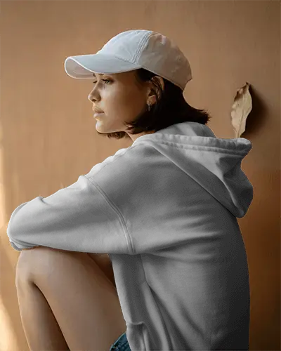 Moody Outdoor Hoodie Mockup Female Model Wearing Cap Sitting Against Earth Toned Wall In Natural Light 0530