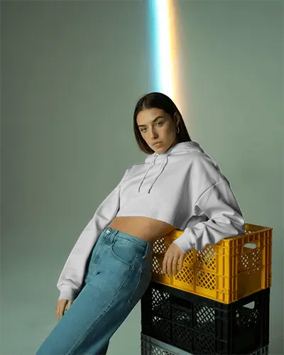 Edgy Studio Cropped Hoodie Mockup Female Model Leaning On Yellow Crate With Rainbow Light Effect 0593