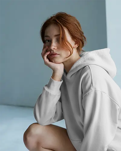 White Hoodie Mockup Female Model Sitting In Soft Blue Studio Moody Natural Lighting Cozy Fit Design On Front