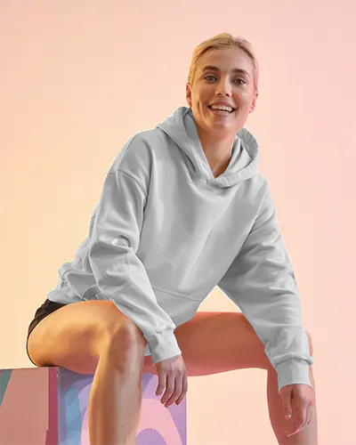 Front View White Hoodie Mockup Smiling Woman Sitting On Painted Box Soft Gradient Background Playful Lighting
