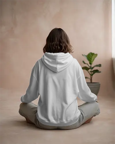 Back View White Hoodie Mockup Woman Sitting Cross Legged Neutral Toned Room Plant In Background Relaxed Natural Light Style