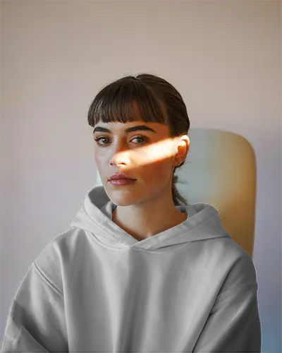 White Hoodie Mockup Front View Woman Sitting In Chair Soft Lighting Shadow On Face Minimalist Background Focus On Chest Logo Relaxed Fit