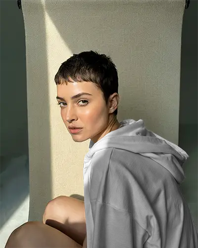 Sunlit Textured Backdrop Hoodie Mockup Female Model Seated In Natural Light Soft Shadows And Warm Tones