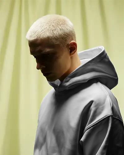 Moody Studio Hoodie Mockup Blonde Male Model Looking Down Against Soft Yellow Curtain Backdrop