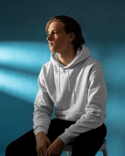 Soft Shadowed Hoodie Mockup Side Lit Male Model In Relaxed Seated Pose Against Blue Background