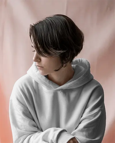 Soft Lighting White Hoodie Mockup Female Model Looking Down In Peach Background Calm And Minimalist Studio Scene 0701