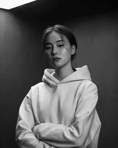 Monochrome Hoodie Mockup Female Model In Soft Top Lighting With Crossed Arms And Neutral Expression