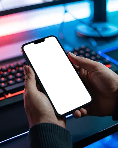 Person Holding Modern Iphone 14 Mockup With Blurred Gaming Keyboard Background For App Preview