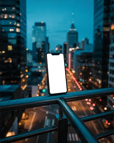 Iphone 14 Mockup On Metal Railing With Blurred City Lights And Blue Hour Skyline Backdrop