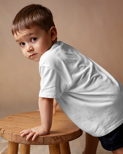 Playful Kid T Shirt Mockup Young Boy In Dark Green Tee Leaning On Wooden Stool Against Warm Neutral Background Adorable And Casual Look