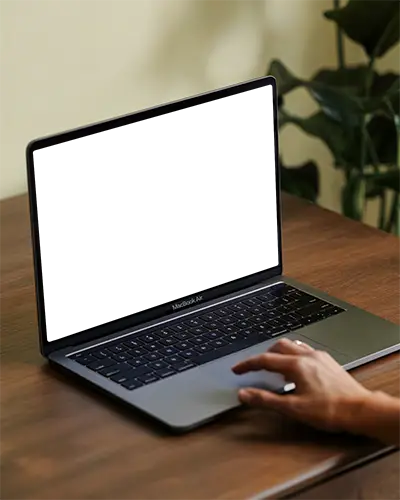 Macbook Air M1 Mockup Hand On Trackpad Wooden Desk Indoor Natural Light Soft Focus Background Green Houseplant Modern Creative Setup