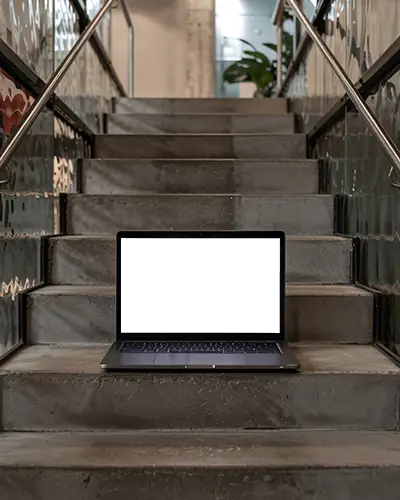 M1 Pro Mockup On Modern Metal Staircase In Industrial Interior With Warm Natural Light
