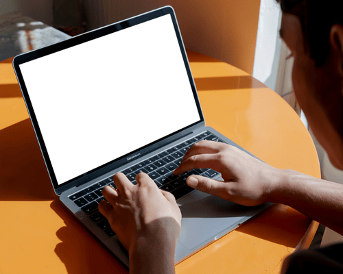 Hands Typing On Macbook Air M1 Placed On Bright Orange Table In Natural Light For A Vibrant Productive Scene