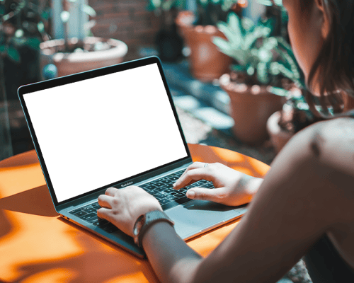 Hands Typing On Macbook Air M2 Placed On Orange Table With Sunlit Potted Plants In Background For Vibrant Outdoor Ambiance