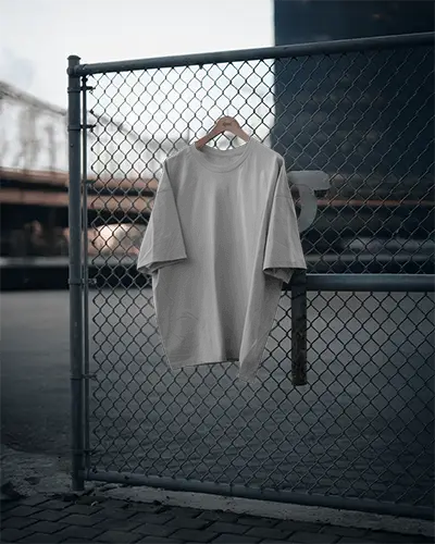 Urban Streetwear Boxy Tshirt Mockup Hanging On Fence With Industrial Backdrop
