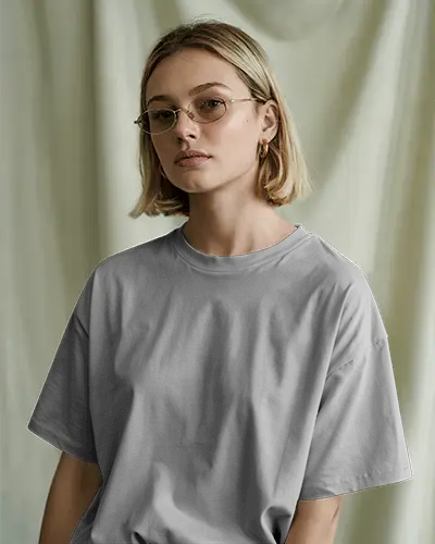 Soft Studio Light T Shirt Mockup Female Model With Blonde Bob Hair And Glasses Wearing Grey Tee In Calm Neutral Setting