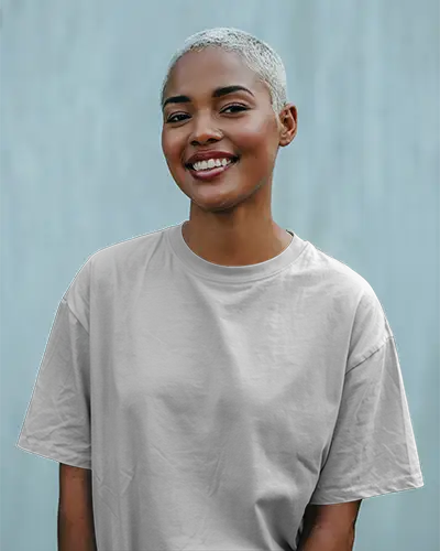 Outdoor T Shirt Mockup Smiling Female Model With Platinum Buzzcut In Grey Tee Standing Against Light Blue Wall