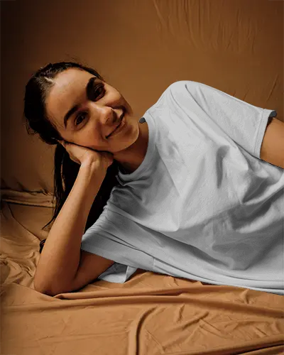 Relaxed Pose T Shirt Mockup Female Model Lying On Brown Fabric With Natural Light