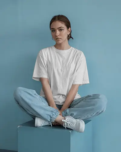 Minimalist Studio T Shirt Mockup Female Model Sitting Cross Legged In Blue Toned Space