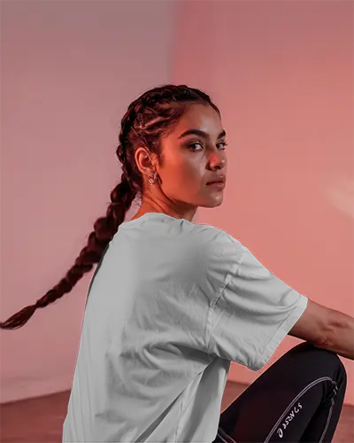 Sporty Lifestyle White Tshirt Mockup Female Model Braided Hair Sitting In Soft Pink Studio Perfect For Fitness Or Athleisure Brand Showcase