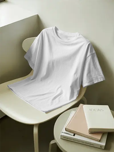 Minimalist Tshirt Mockup Draped On Ivory Chair Next To Books And Round Table In Clean Creative Workspace