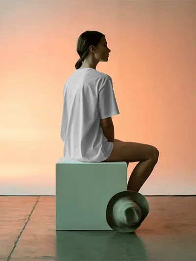 Back View Tshirt Mockup Female Model Sitting On White Block In Sunset Light With Hat On Floor Soft Shadow Scene