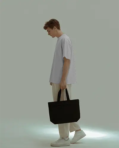 Modern Minimalist Tshirt Mockup With Male Model Holding Black Tote In Muted Studio Light