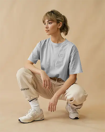 White Tshirt Mockup Female Model Crouching Beige Joggers Neutral Backdrop Streetwear Style Relaxed Athleisure Aesthetic