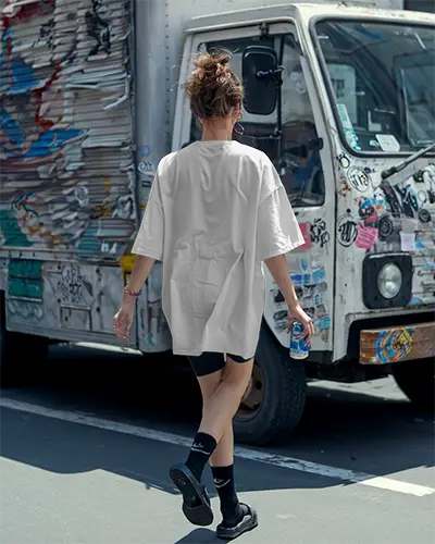 Urban Streetwear Boxy T Shirt Mockup Female Model Walking With Can In Hand In Front Of Graffiti Truck Edgy Casual Scene