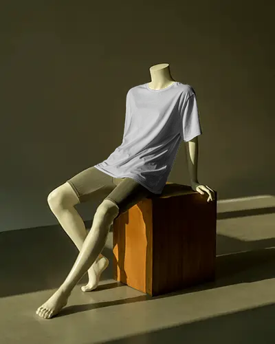 Moody Display T Shirt Mockup Minimal Mannequin Seated On Wood Block In Warm Spotlight