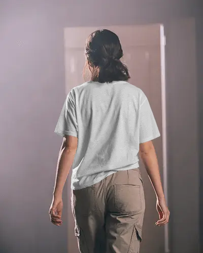 Indoor Tshirt Mockup Female Model Back View Casual Stance Light Through Doorway Soft Mood