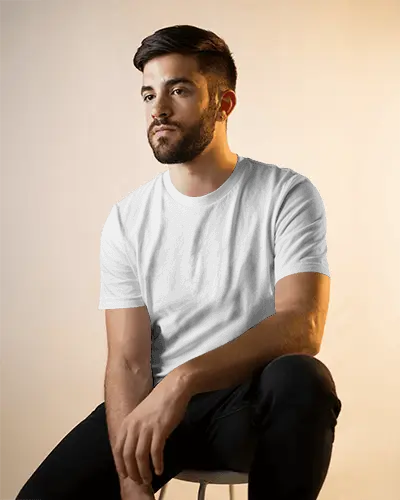 Seated Male Model T Shirt Mockup In Soft Golden Light With Casual Pose And Neutral Backdrop