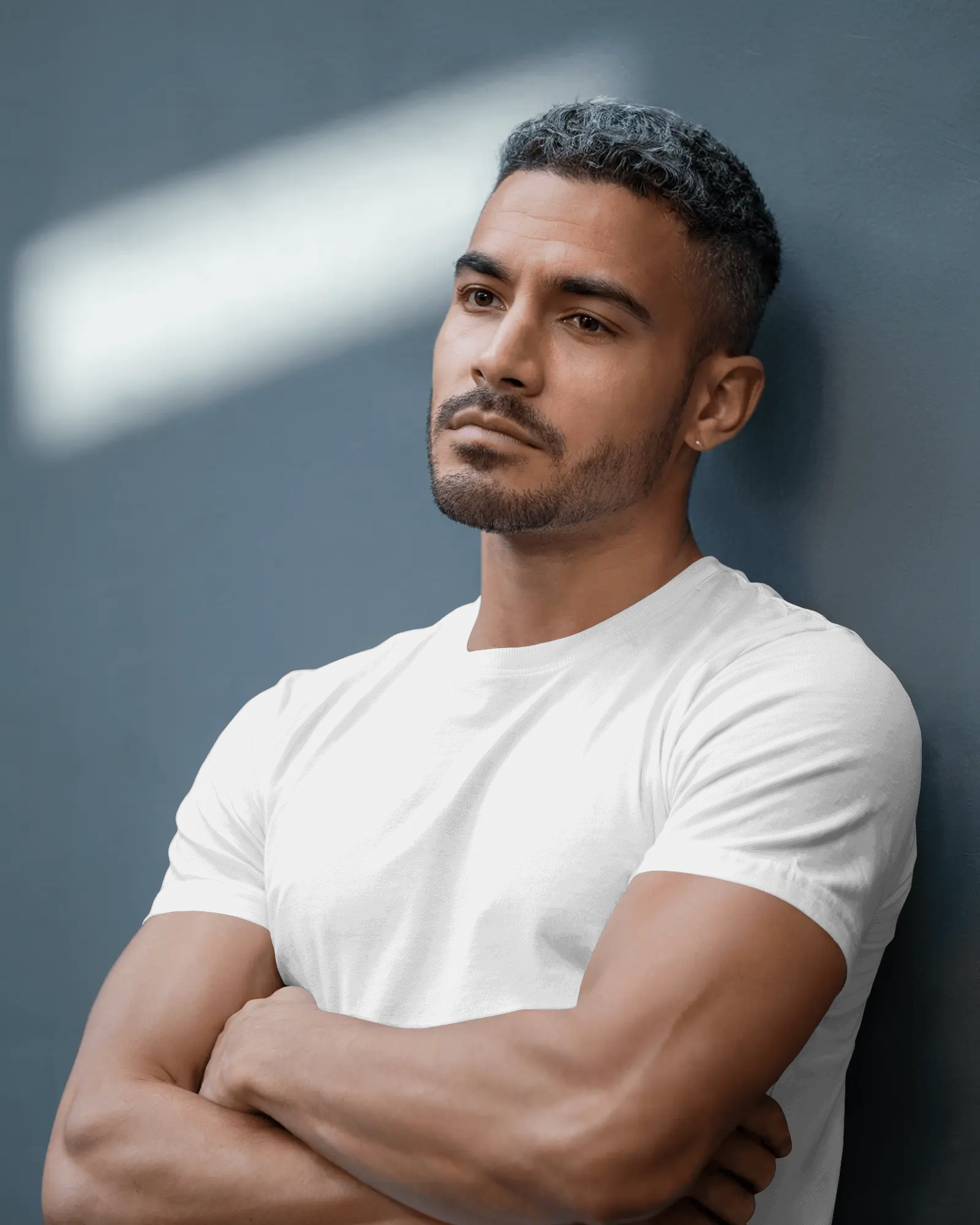 Modern Studio T Shirt Mockup Male Model Leaning Against Wall In Natural Lighting Calm Expression
