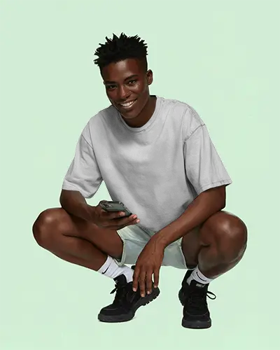 Crouching T Shirt Mockup Male Model Smiling Holding Smartphone In Casual Streetwear Style