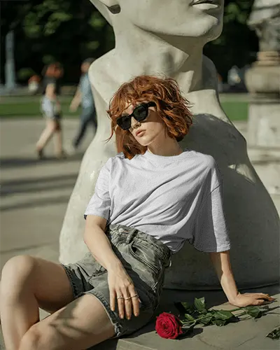 outdoor-fashion-t-shirt-mockup-woman-sitting-by-sculpture-holding-rose-in-sunlight