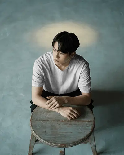moody-studio-t-shirt-mockup-male-model-sitting-on-wooden-stool-under-spotlight-minimal-background