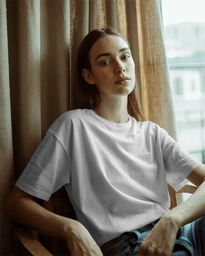 relaxed-indoor-t-shirt-mockup-female-model-sitting-by-window-in-soft-daylight-with-graphic-print