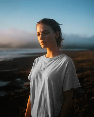 golden-hour-beach-t-shirt-mockup-female-model-gazing-serenely-sunset-lighting-tranquil-atmosphere