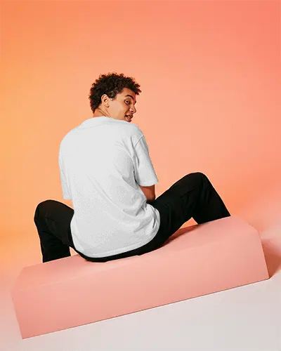 Back View Male T Shirt Mockup Model Seated On Block Looking Over Shoulder In Warm Gradient