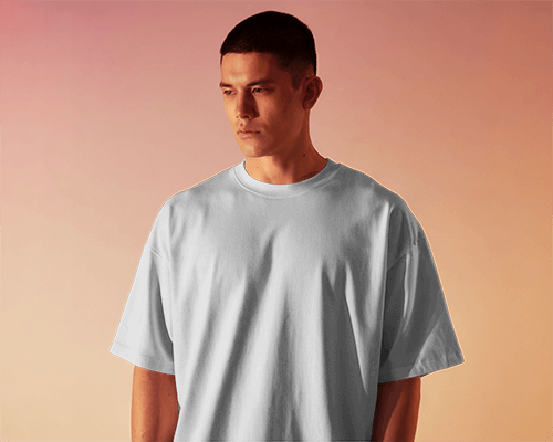 Soft Gradient Background Mockup Front View Of Blank Oversized T Shirt On Male Model Looking Downward With Relaxed Expression Against Warm Toned Backdrop Showcasing Simple Yet Stylish Look